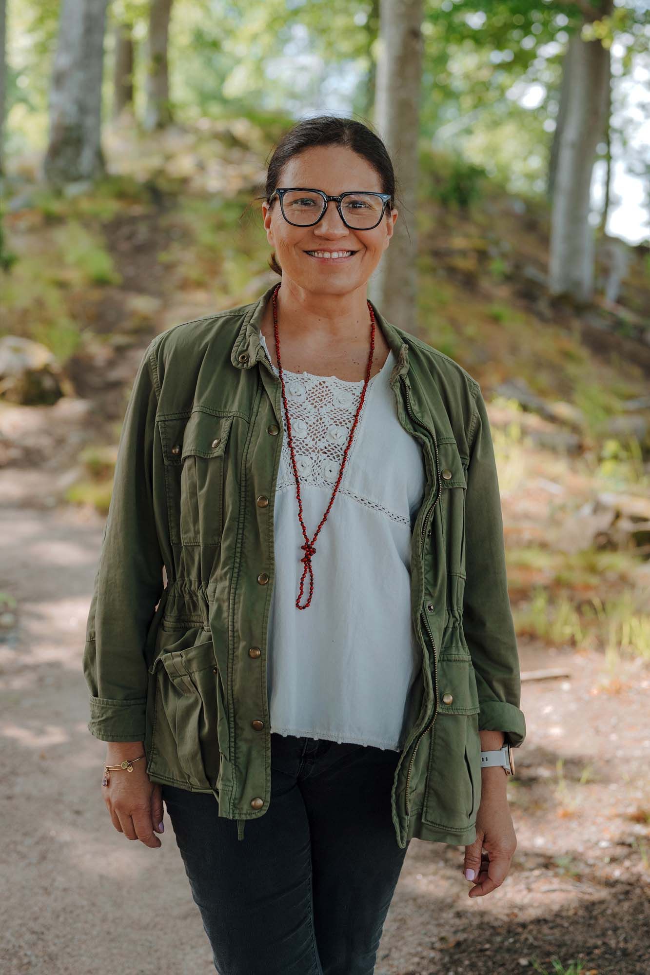 IKEA co-worker Antonia smiles and stands on a path on a sunny day with trees in the background.