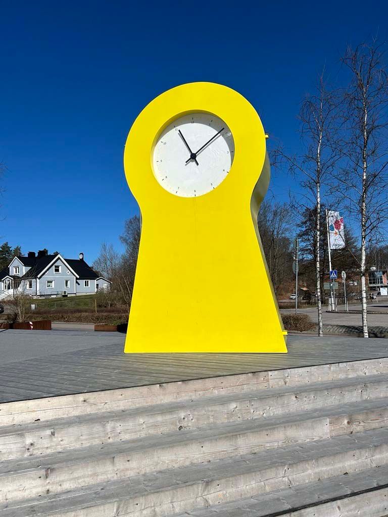 A large yellow PS clock outside the IKEA museum near some steps.