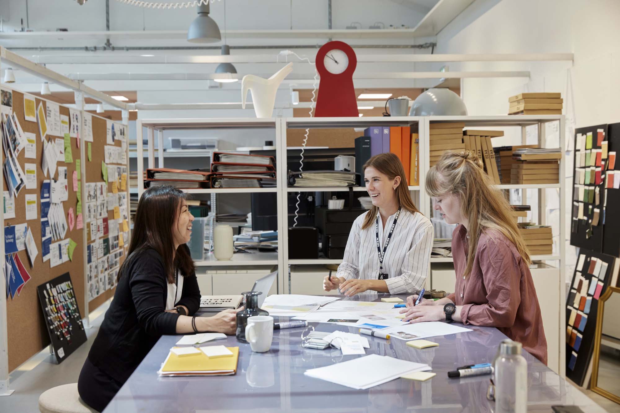 Three people chat while sat round a work desk in the offices of IKEA of Sweden.