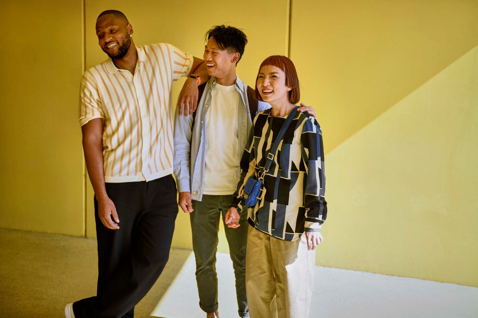 Three people stand in front of a yellow wall, smiling.