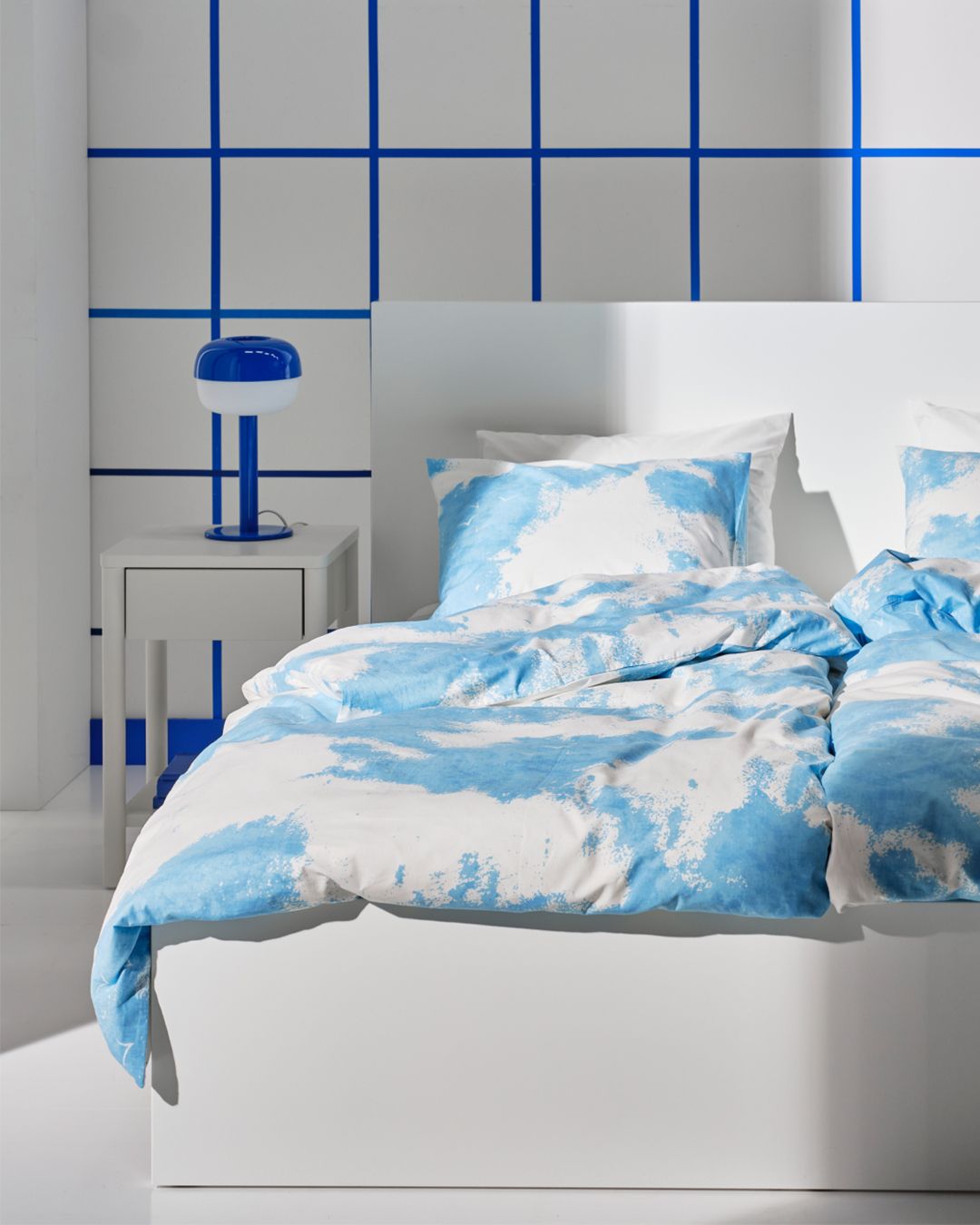 The cutout of an ÄNGSVITVINGE duvet and pillowcase with clouds transforms into a blue and white roomset in the background.