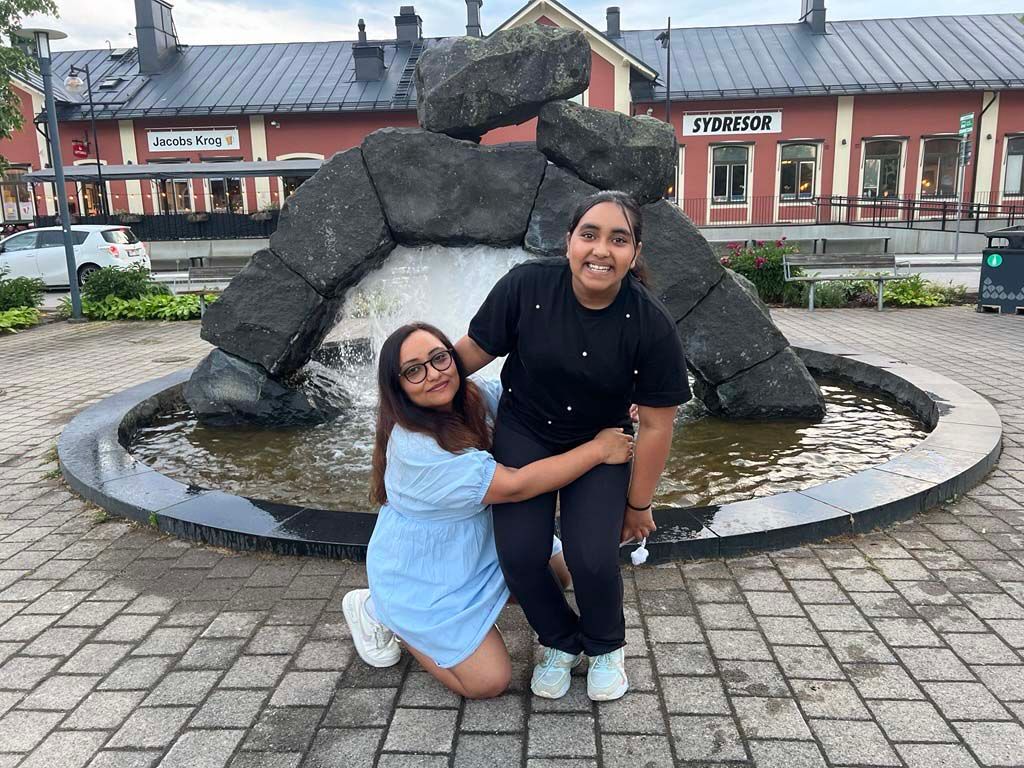 Shaveta kneels in front of a fountain in Älmhult with her child. 