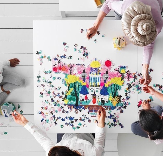 Overhead view of a group of people assembling a colourful jigsaw puzzle on a white table.