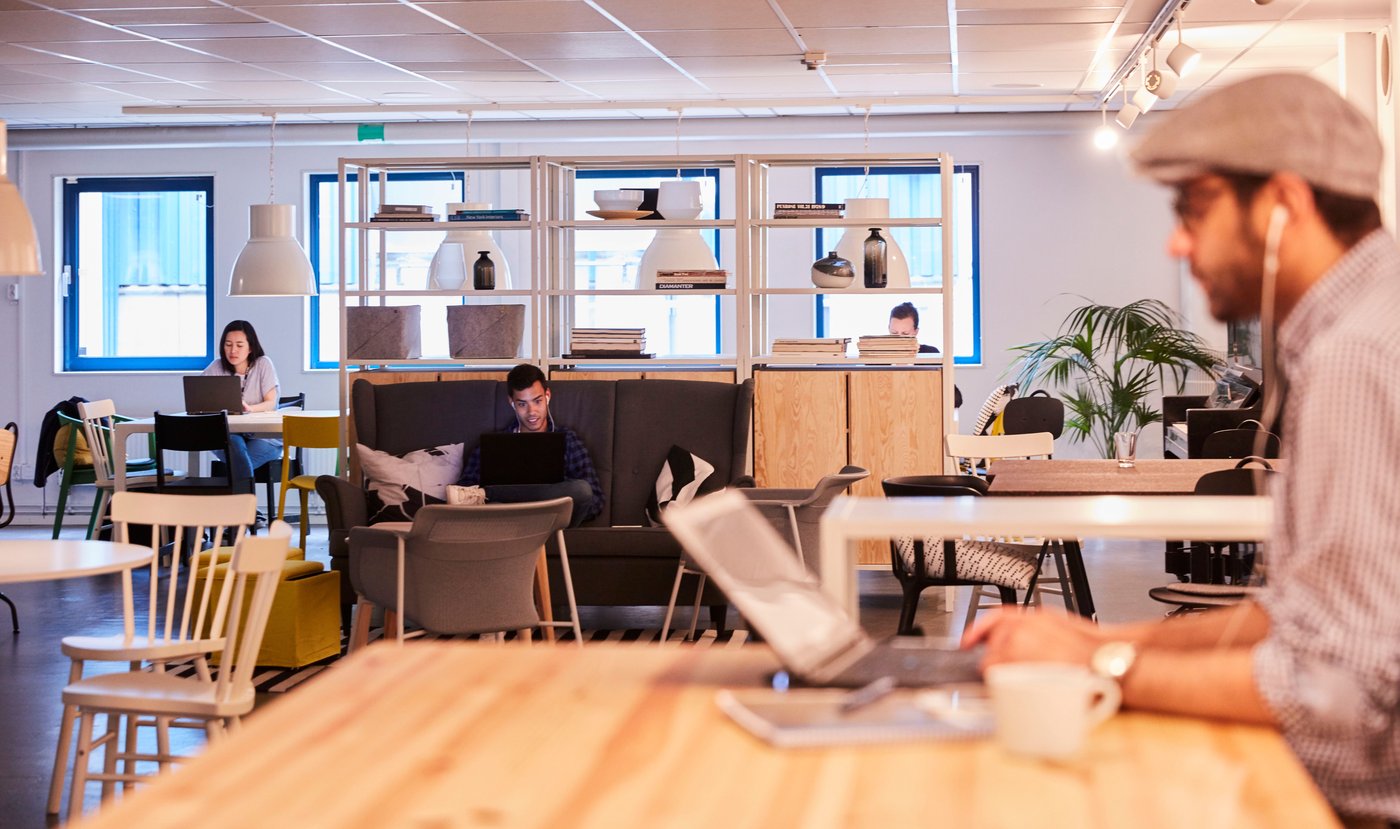A room with chairs and tables and people sitting working on laptops.