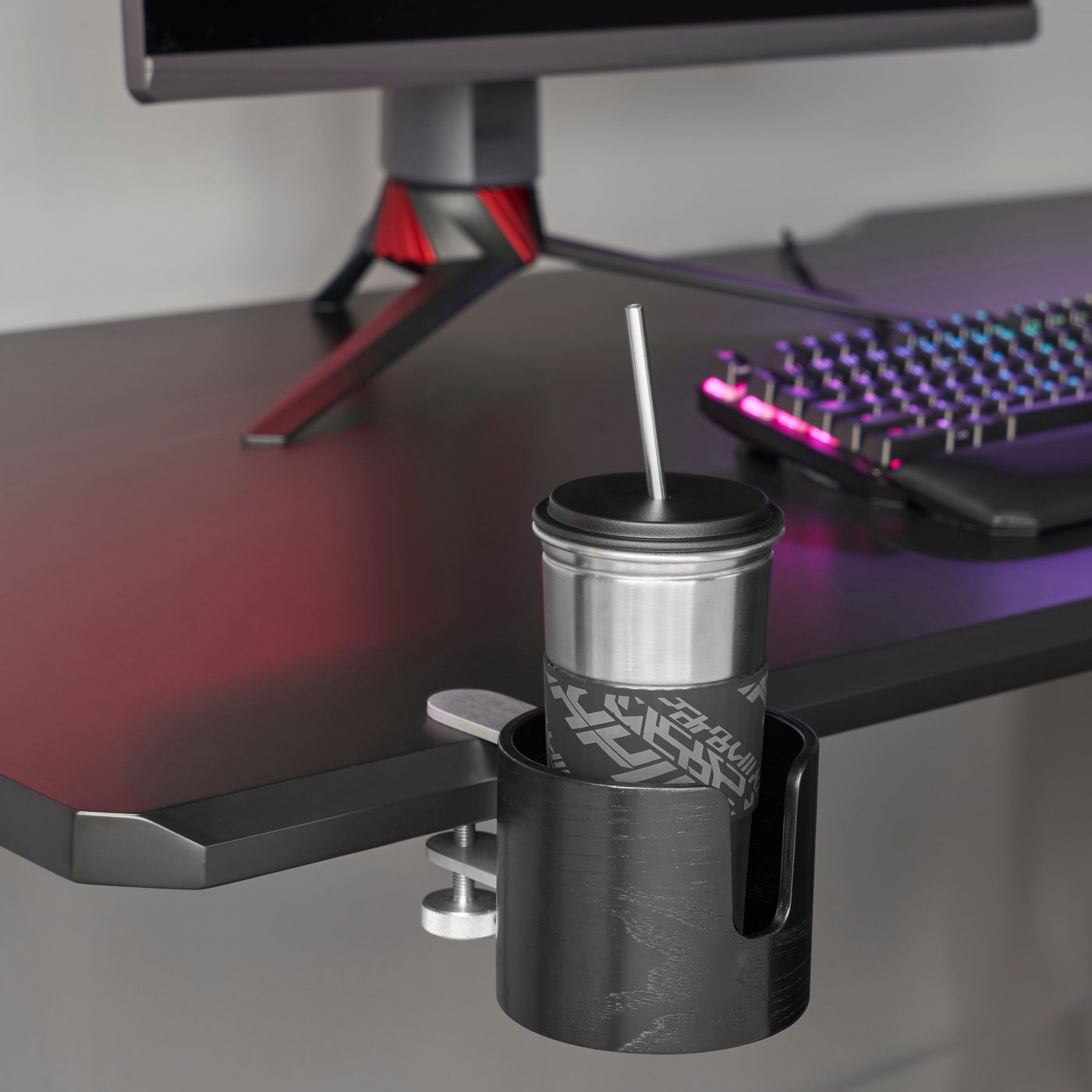 A cup with a straw sits in a holder on a black gaming desk.