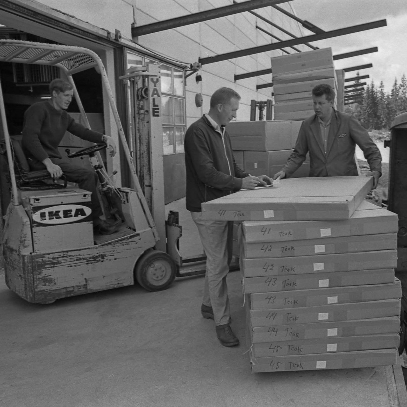 A photograph from the mid-sixties of two men unloading boxes next to a forklift at the quay at DC Älmhult.