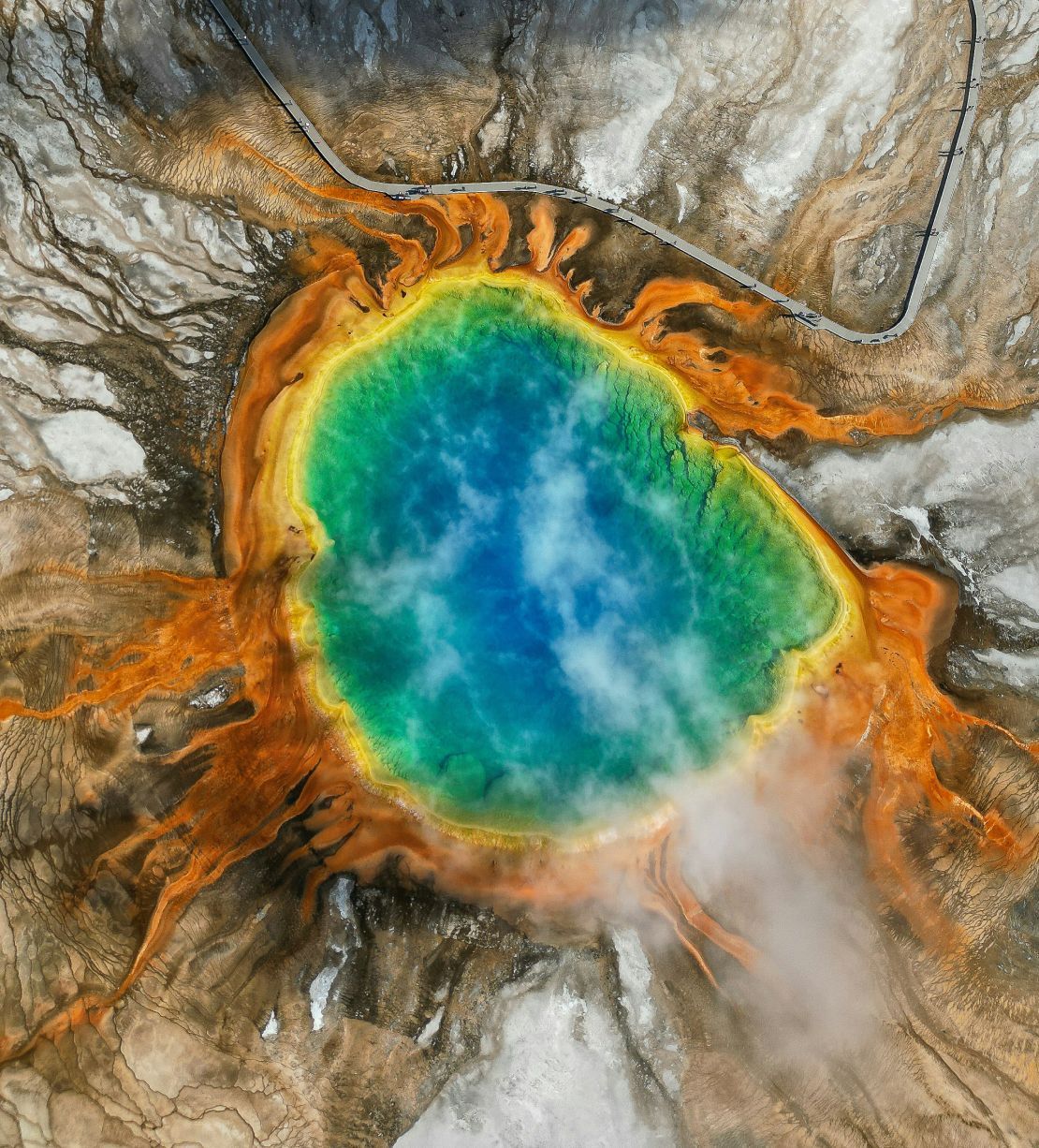 An overhead shot of an almost circular lake in a crater. The blue water is rimmed with yellow and orange earth.
