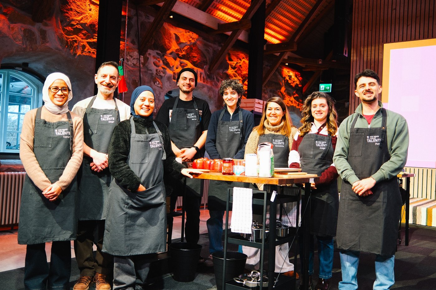 A group of people wearing aprons, standing by a table with cooking ingredients.