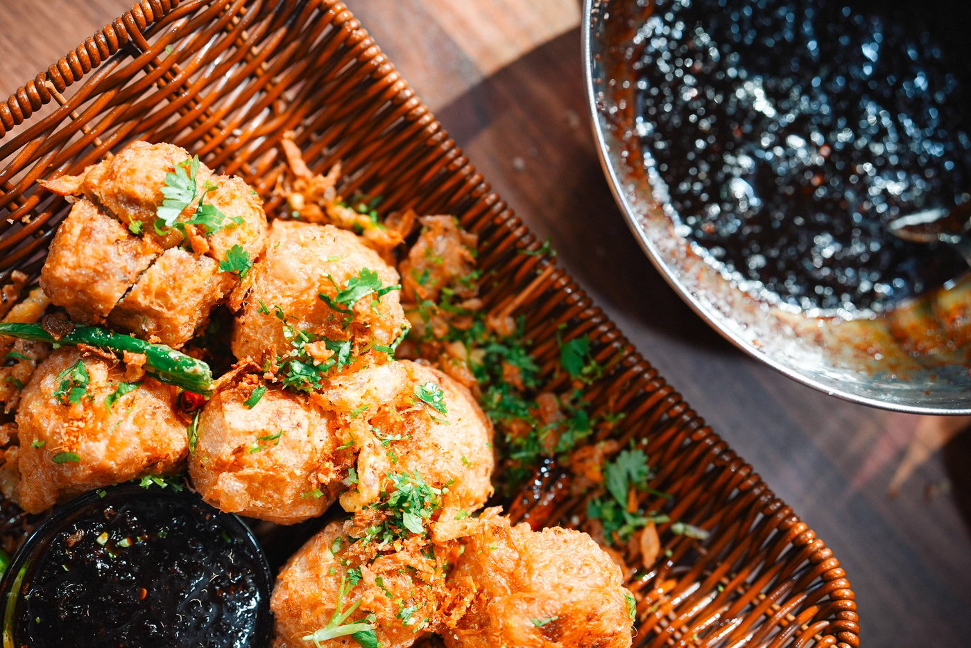 A woven tray filled with golden, crispy stuffed fried tofu, accompanied by lime wedges and a small bowl of sambal soy sauce. Nearby, a larger bowl contains sauce and a spoon, creating an appetising display.