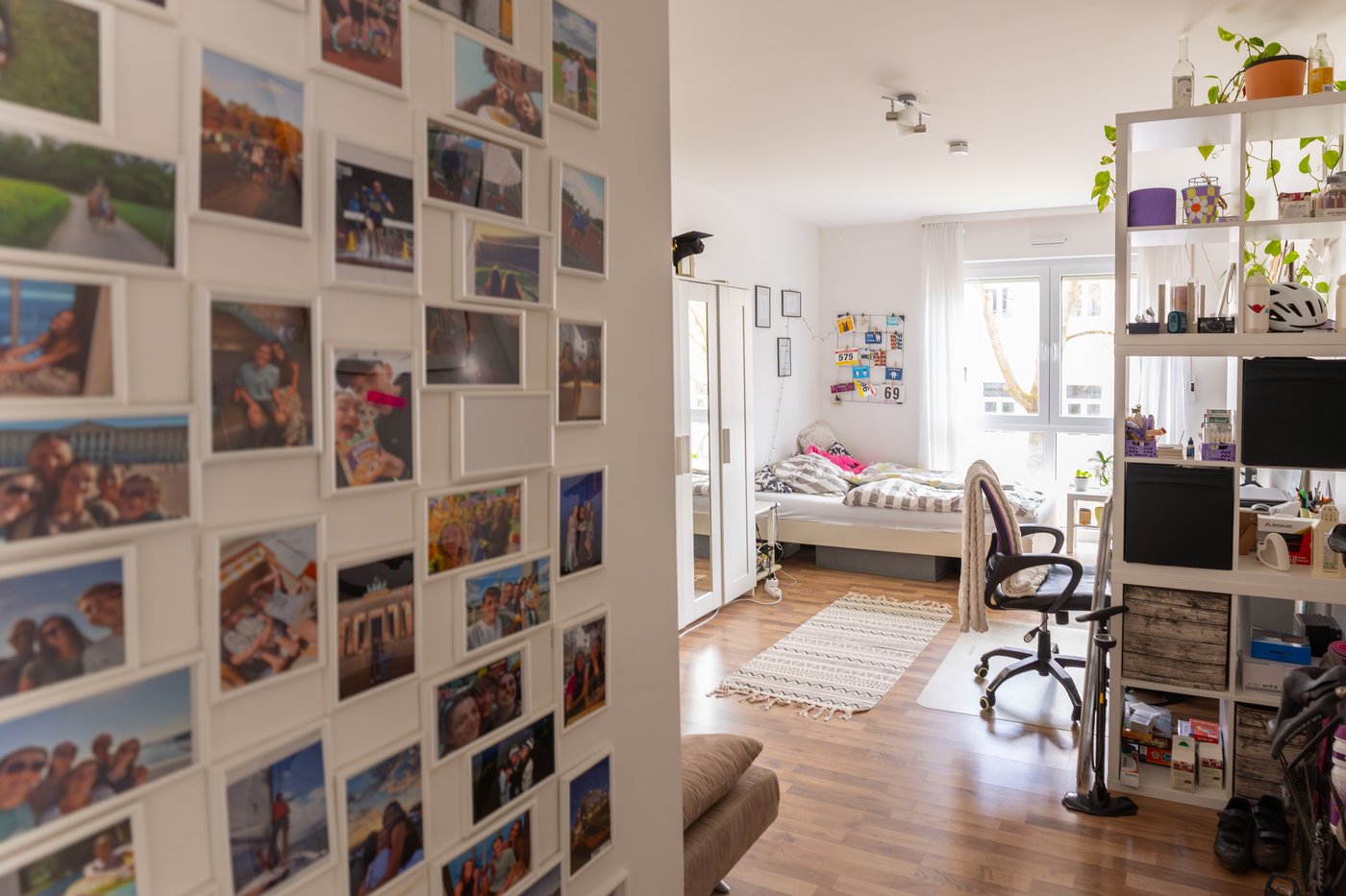 A view into a room with white walls, with a gallery wall filled with photographs, open shelving and a bed.