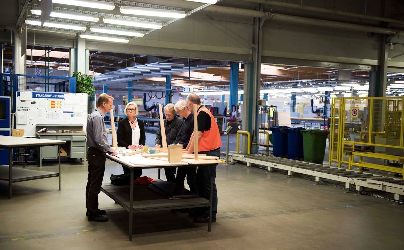 Designers and engineers look at sketches and prototypes in a workshop.
