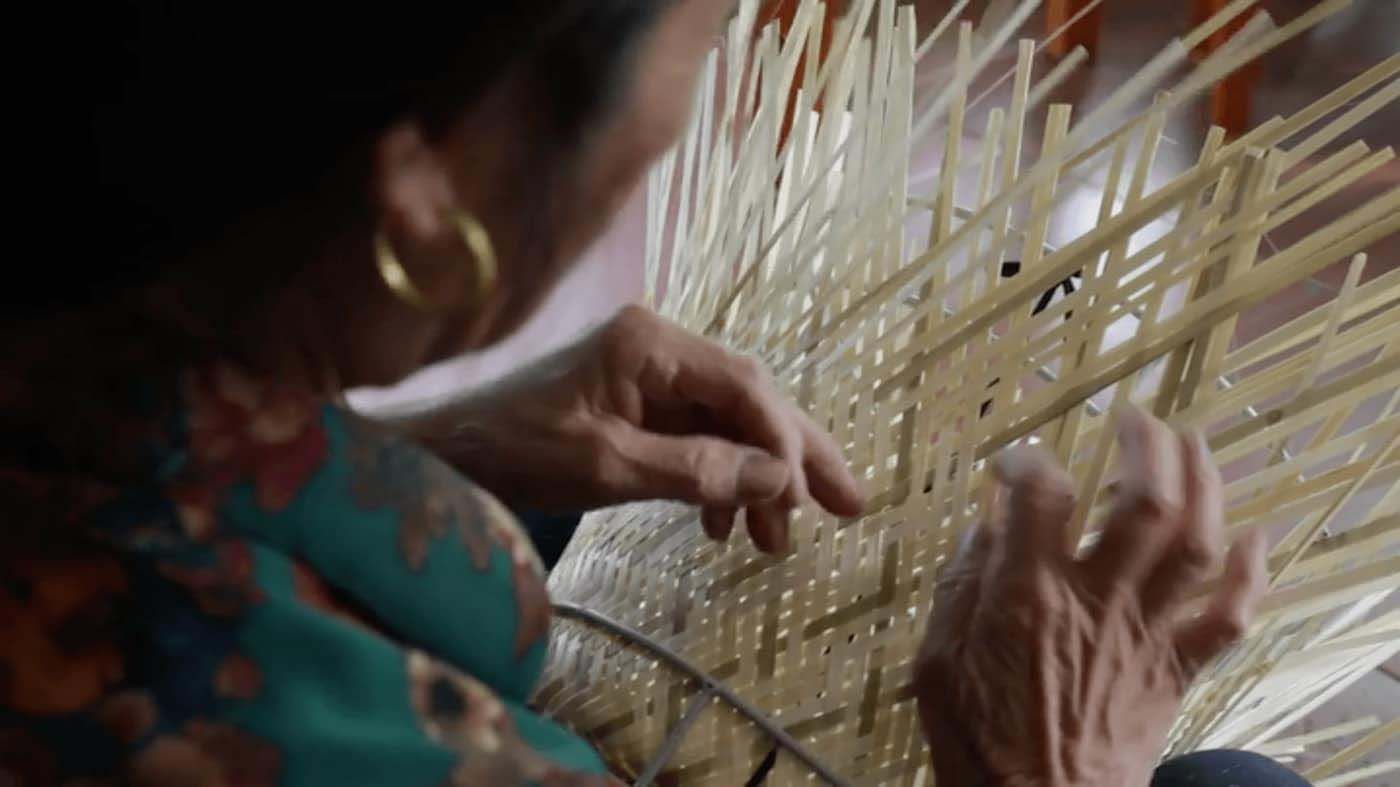 A person's weaving strands of bamboo into a product.