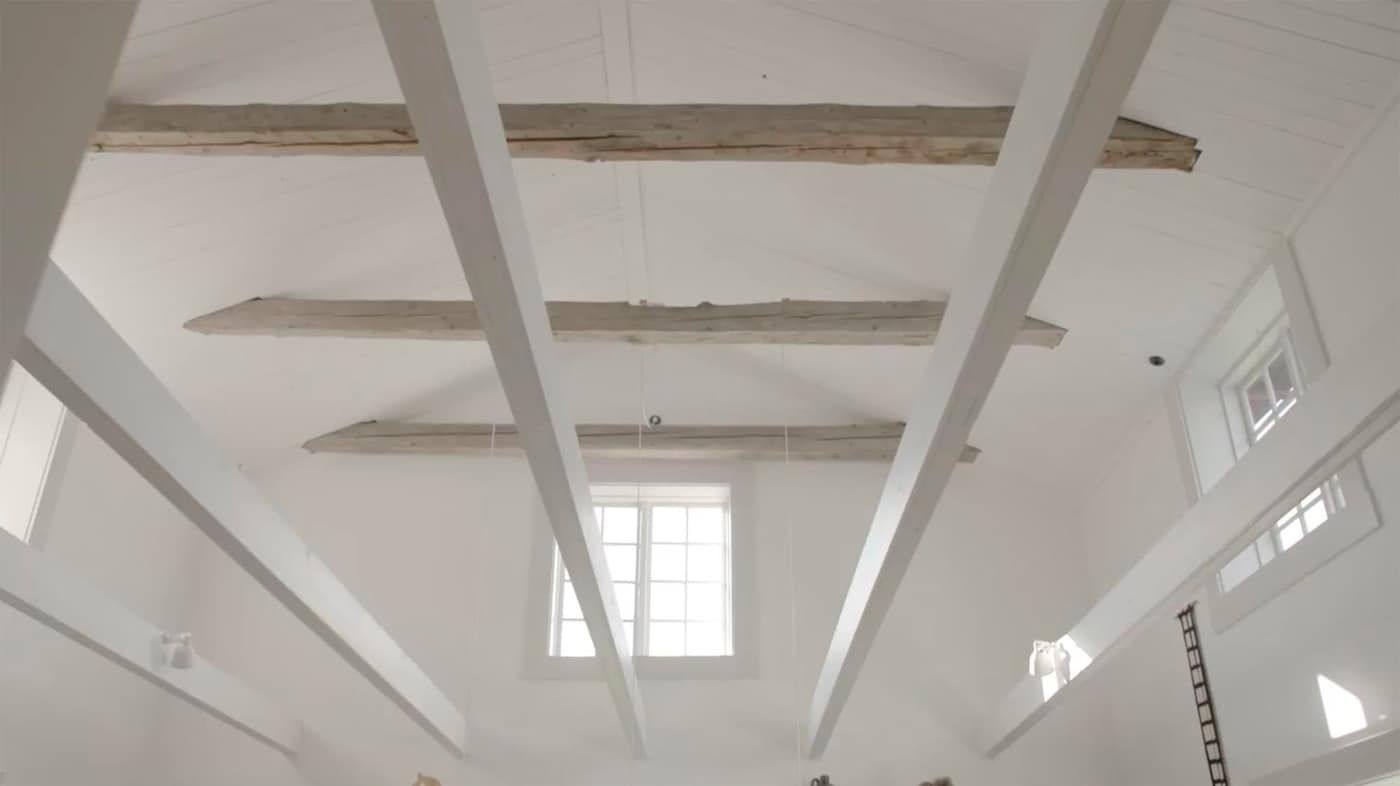 View of a room's ceiling with high windows and exposed beams.