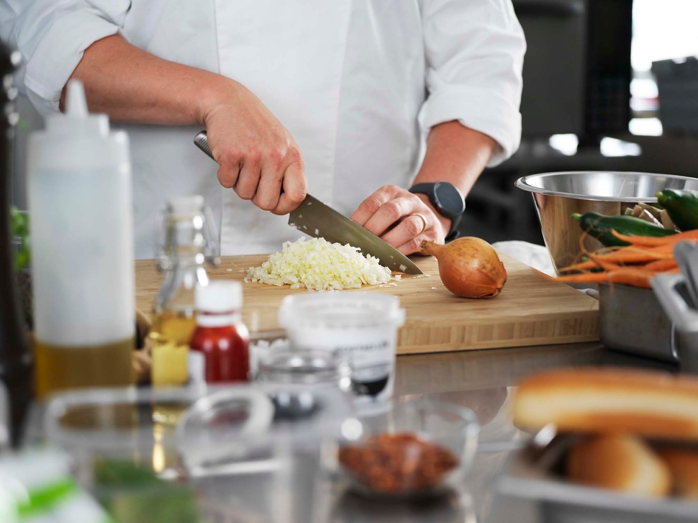 A cropped image of a chef holding a knife and cutting onions on a wood chopping board.