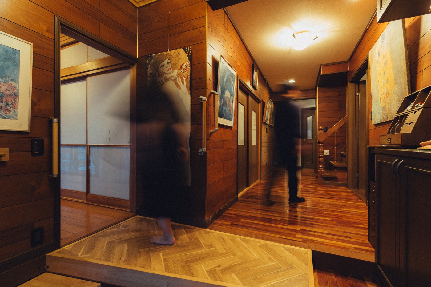 A blurred person walks through a hallway with wooden floors and walls.