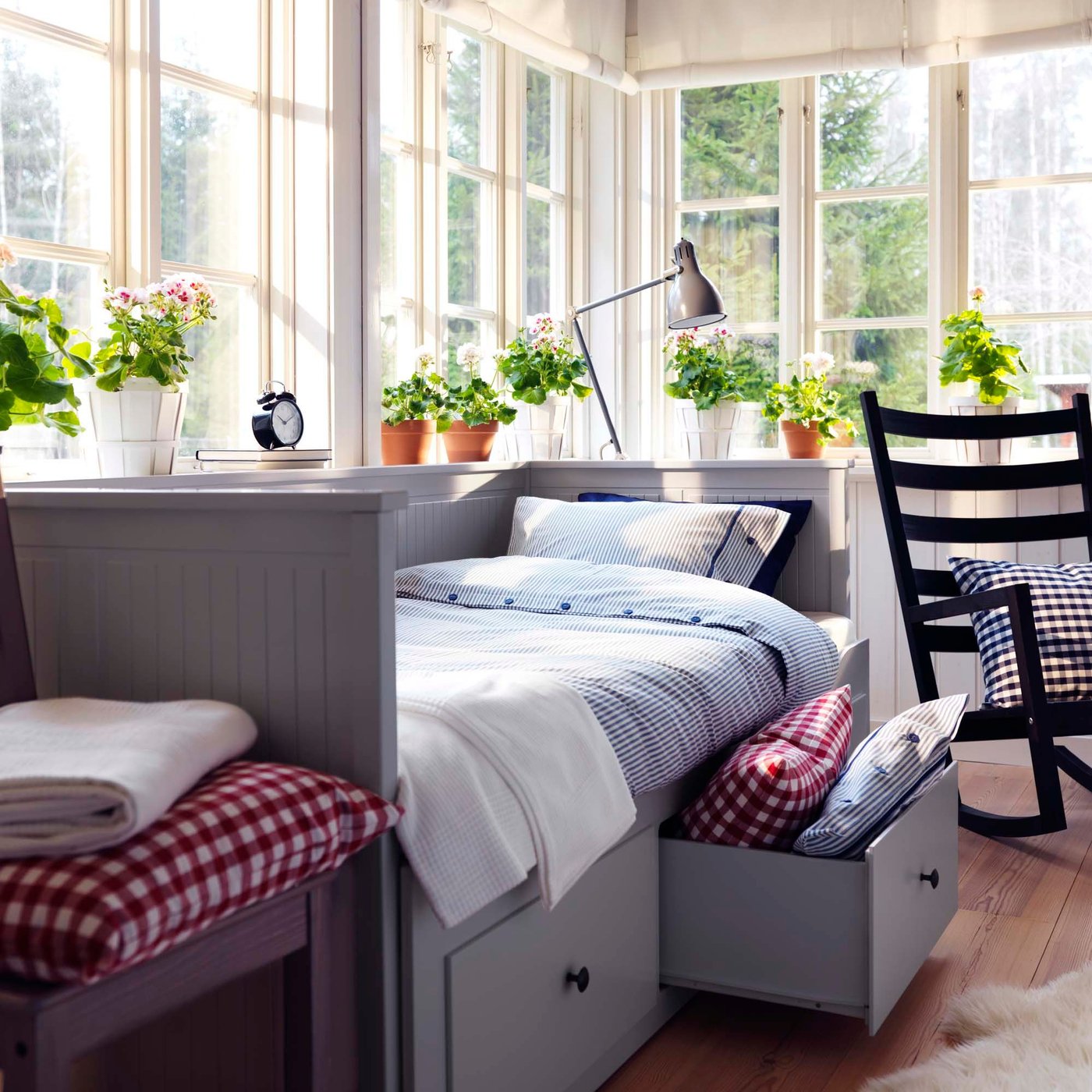 A grey HEMNES daybed with bedding and an open drawer, positioned in front of windows.