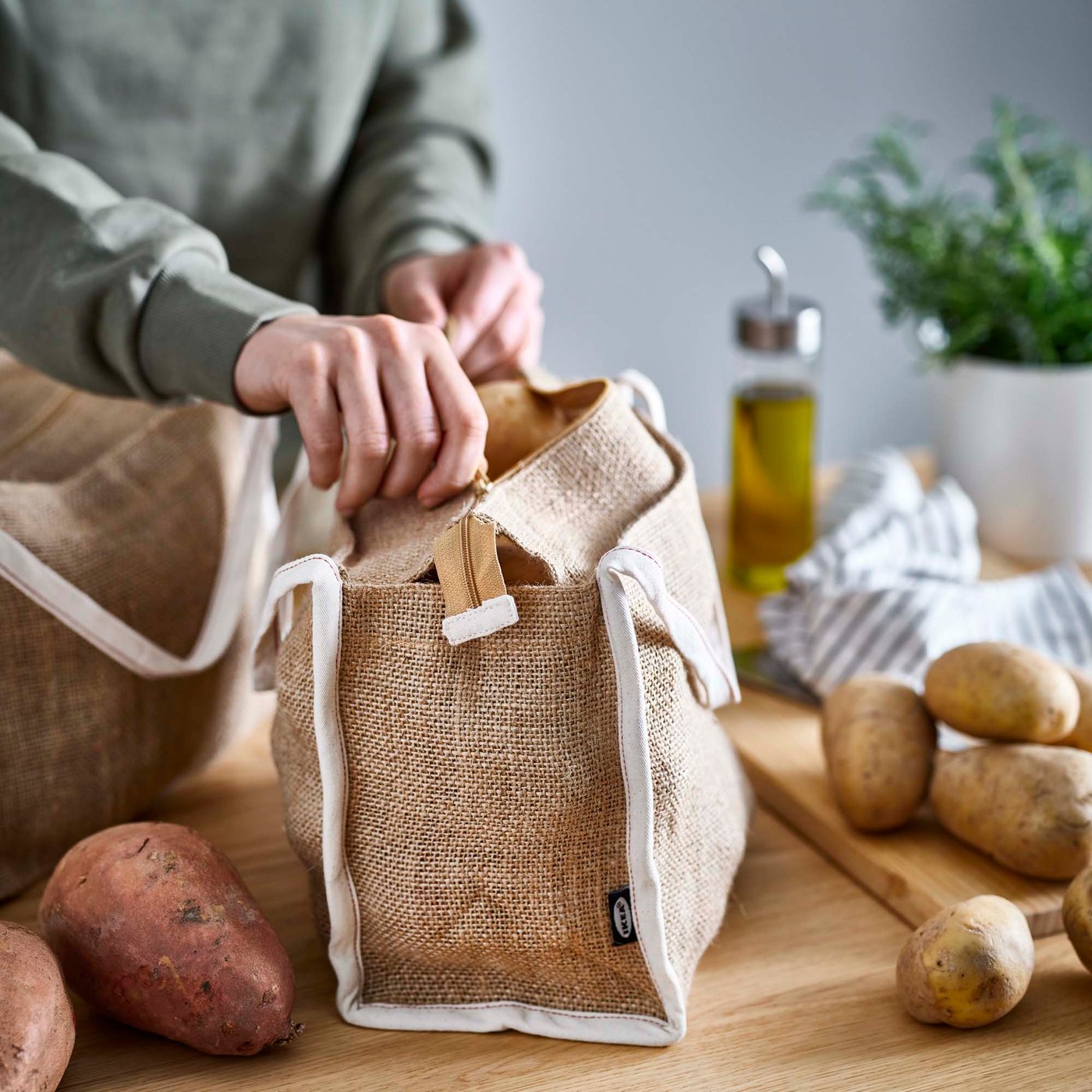 A person zips up a jute bag filled with potatoes.