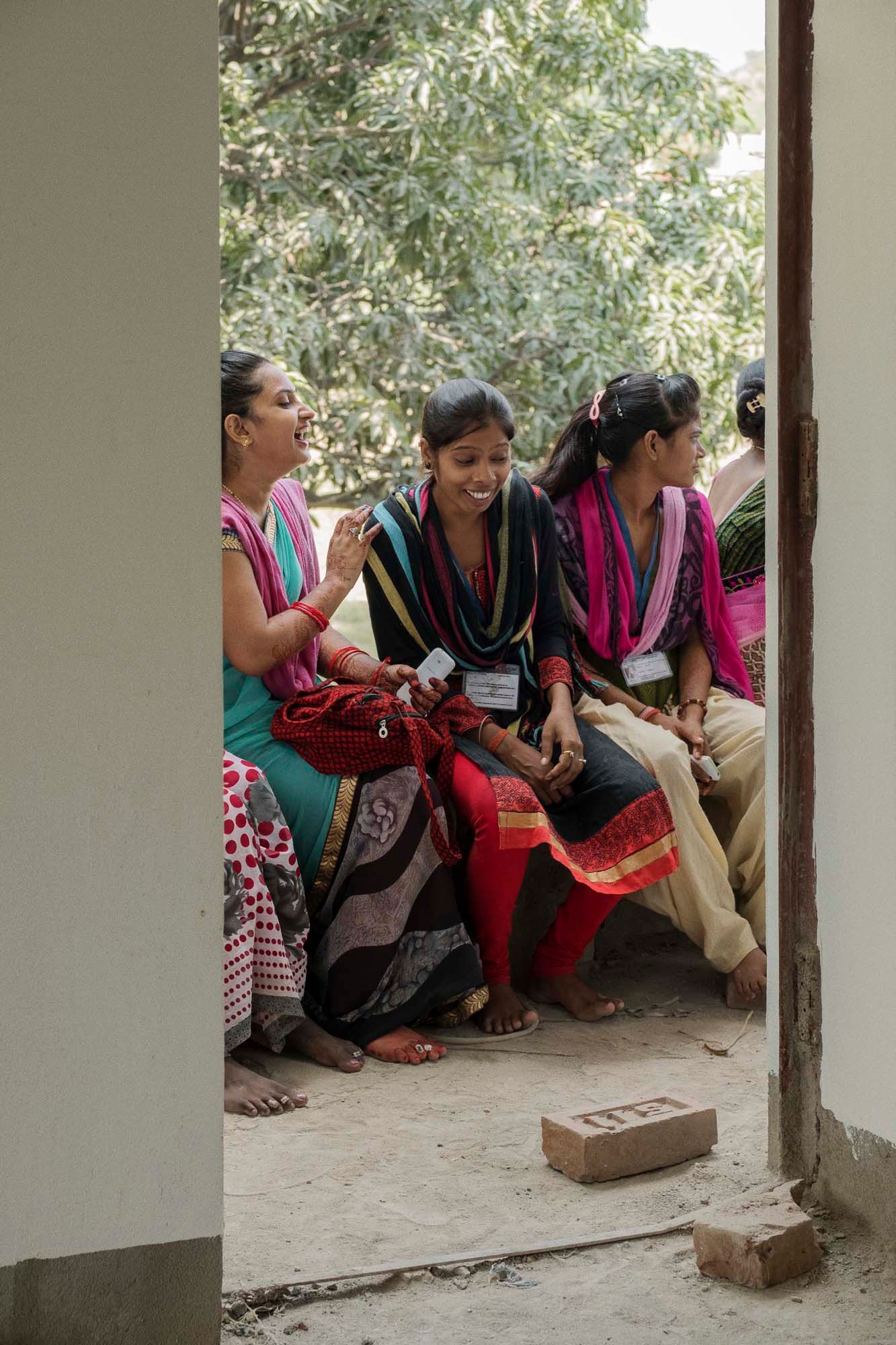 A group of women, seen through a doorway. They are sitting closely together on a bench, talking and laughing.