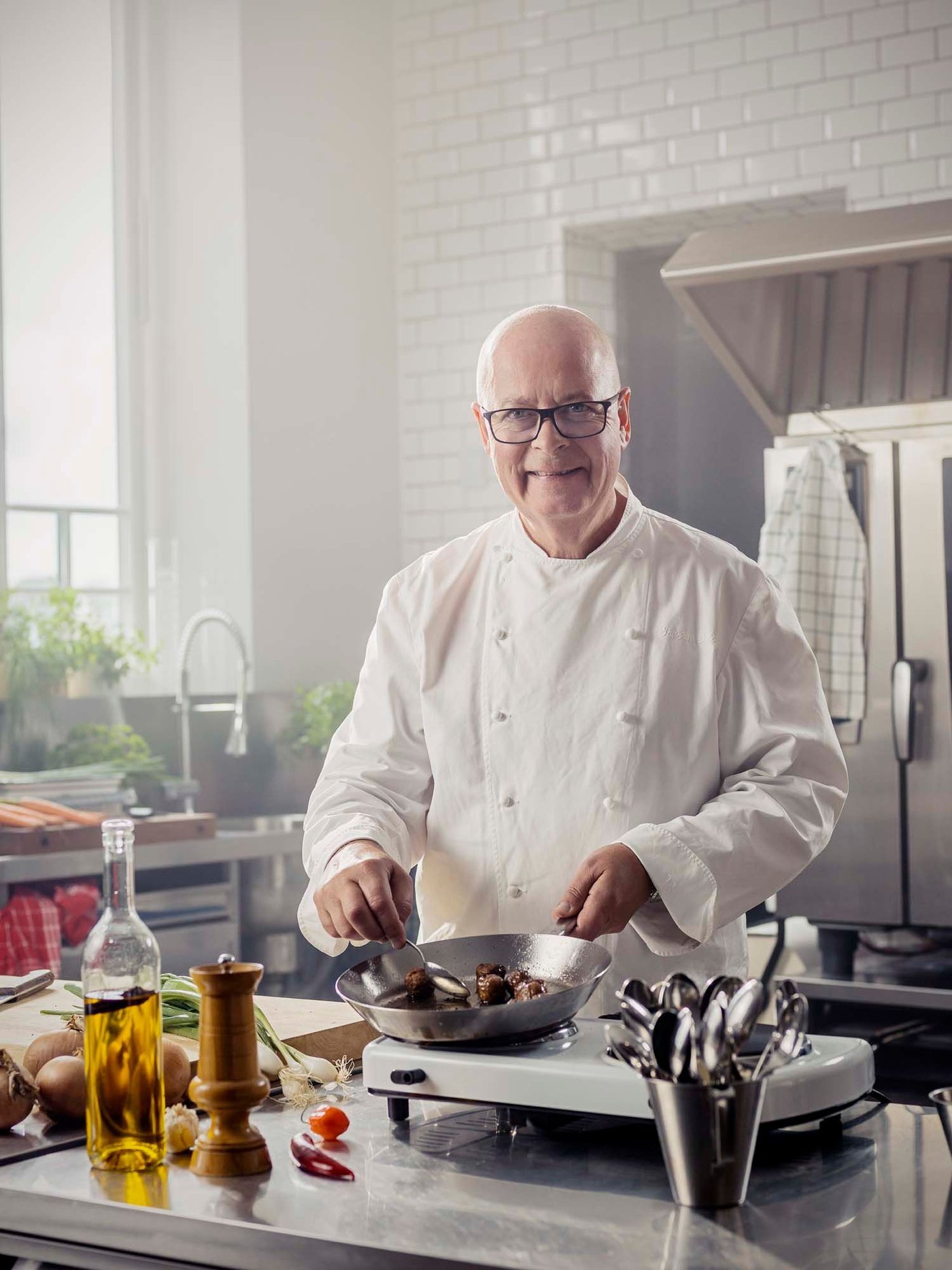 Chef Severin Sjöstedt stands in a kitchen. He smiles at the camera as he cooks meatballs.