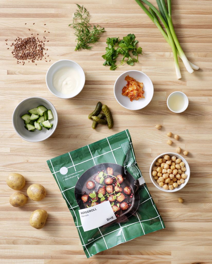 A package of HUVUDROLL plant balls on a wooden worktop, surrounded by vegetables, herbs and sauces.