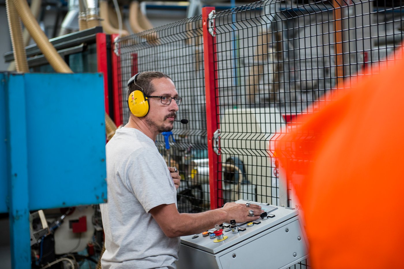 A man operates machinery in a factory environment. He is wearing protective headphones.
