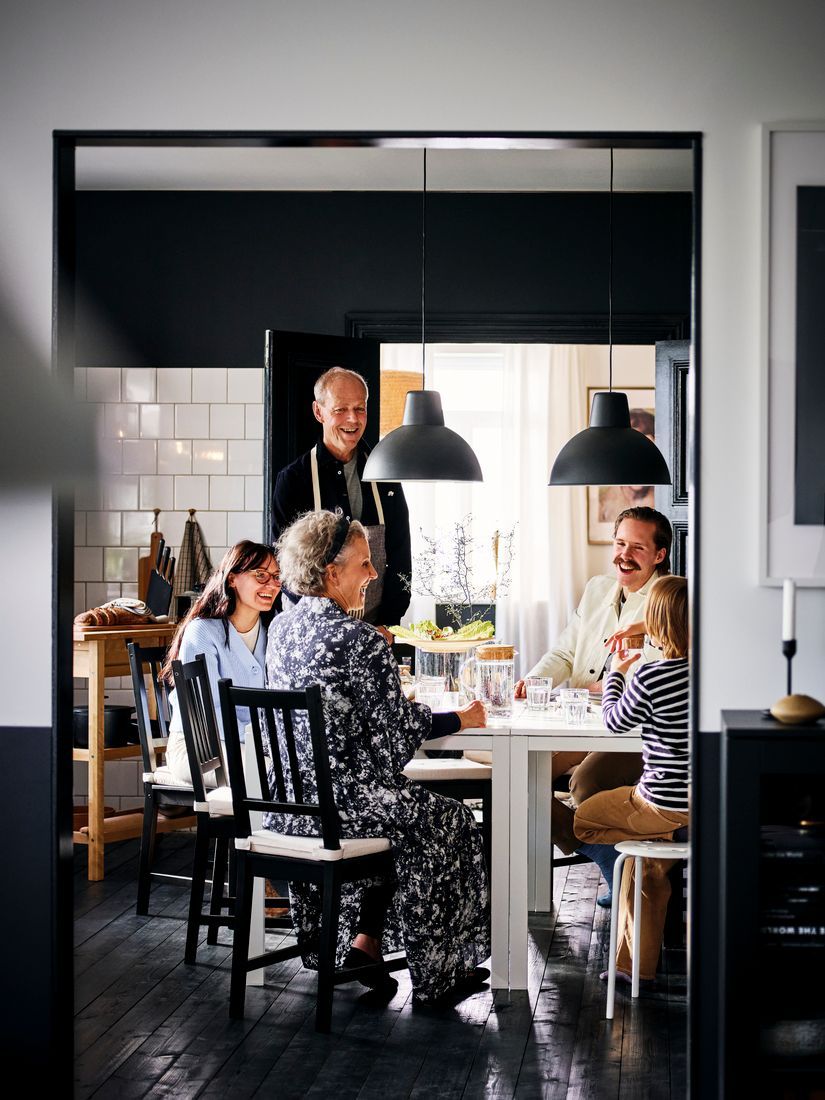 A family of five gathered around a white dining table in a dining area with black-painted hardwood floors and white-tiled walls.