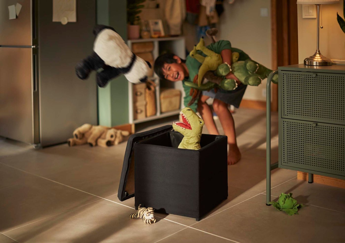 A boy picks up toys and throws them into a box. He is laughing.