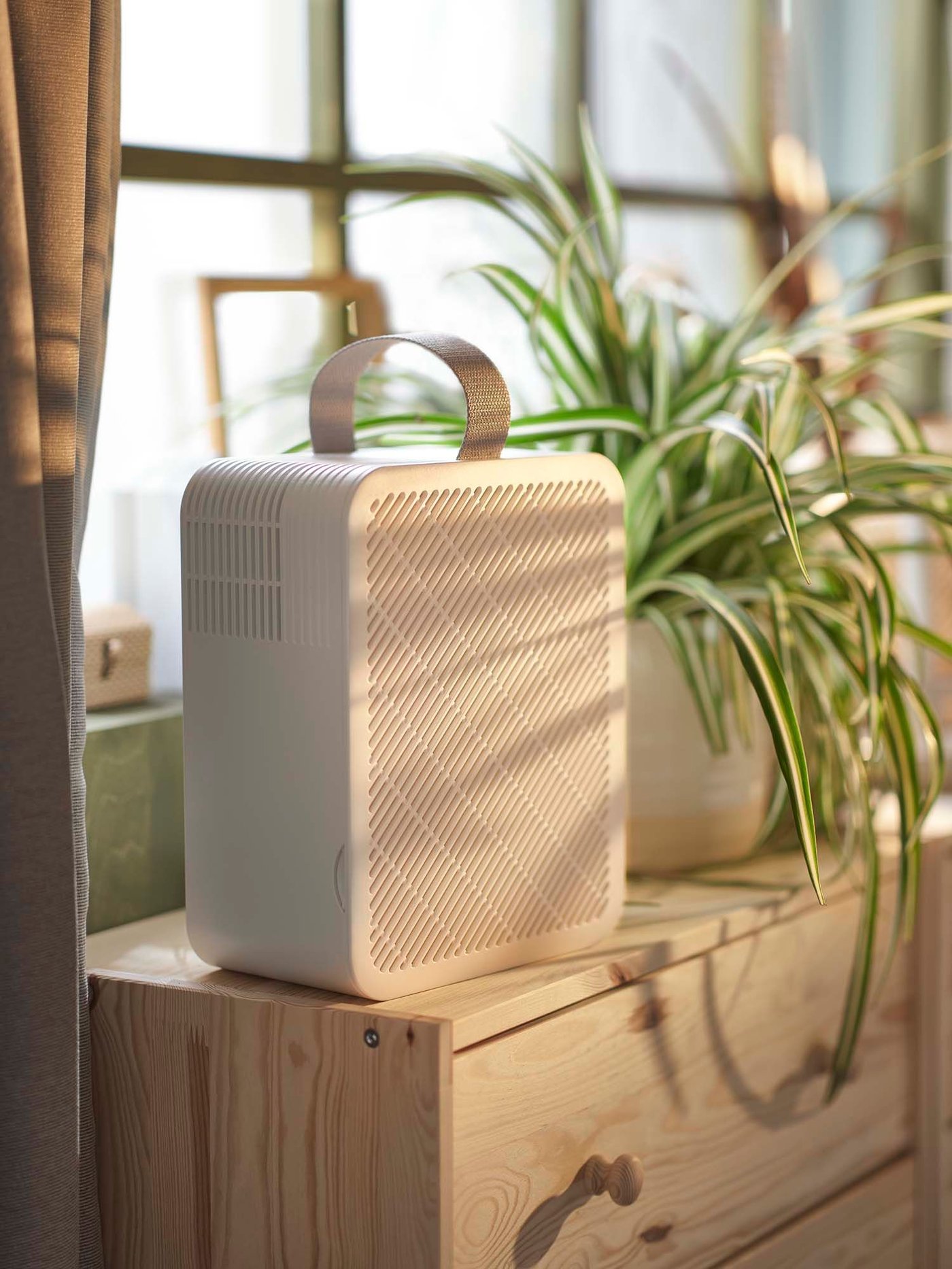 An UPPÅTVIND air purifier stands on a chest of drawers, next to a vase of flowers.