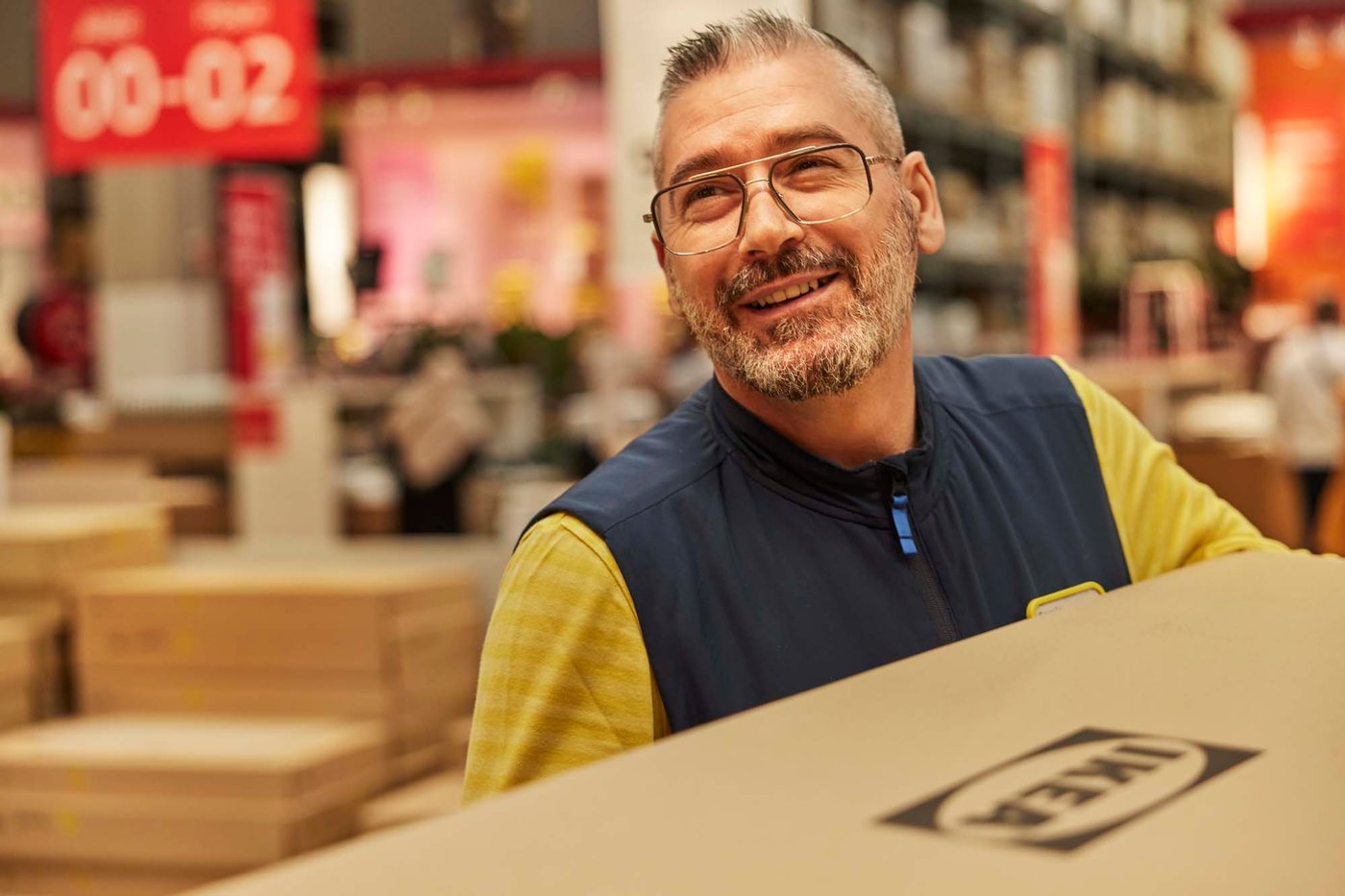 A person smiles while carrying an IKEA flatpack box.