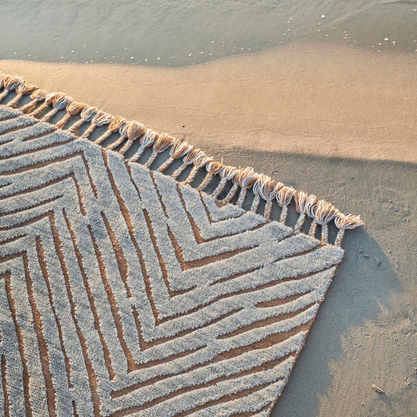 A patterned KLAPPERSTARR rug with fringed edges on a sand background.