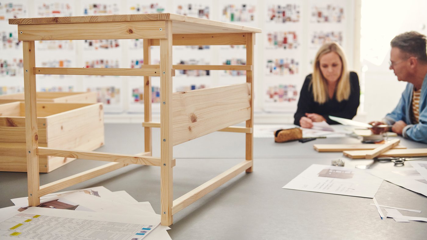 Two IKEA co-workers sit together looking at sketches, with a KRONÖREN chest of drawers prototype on the table in the foreground.