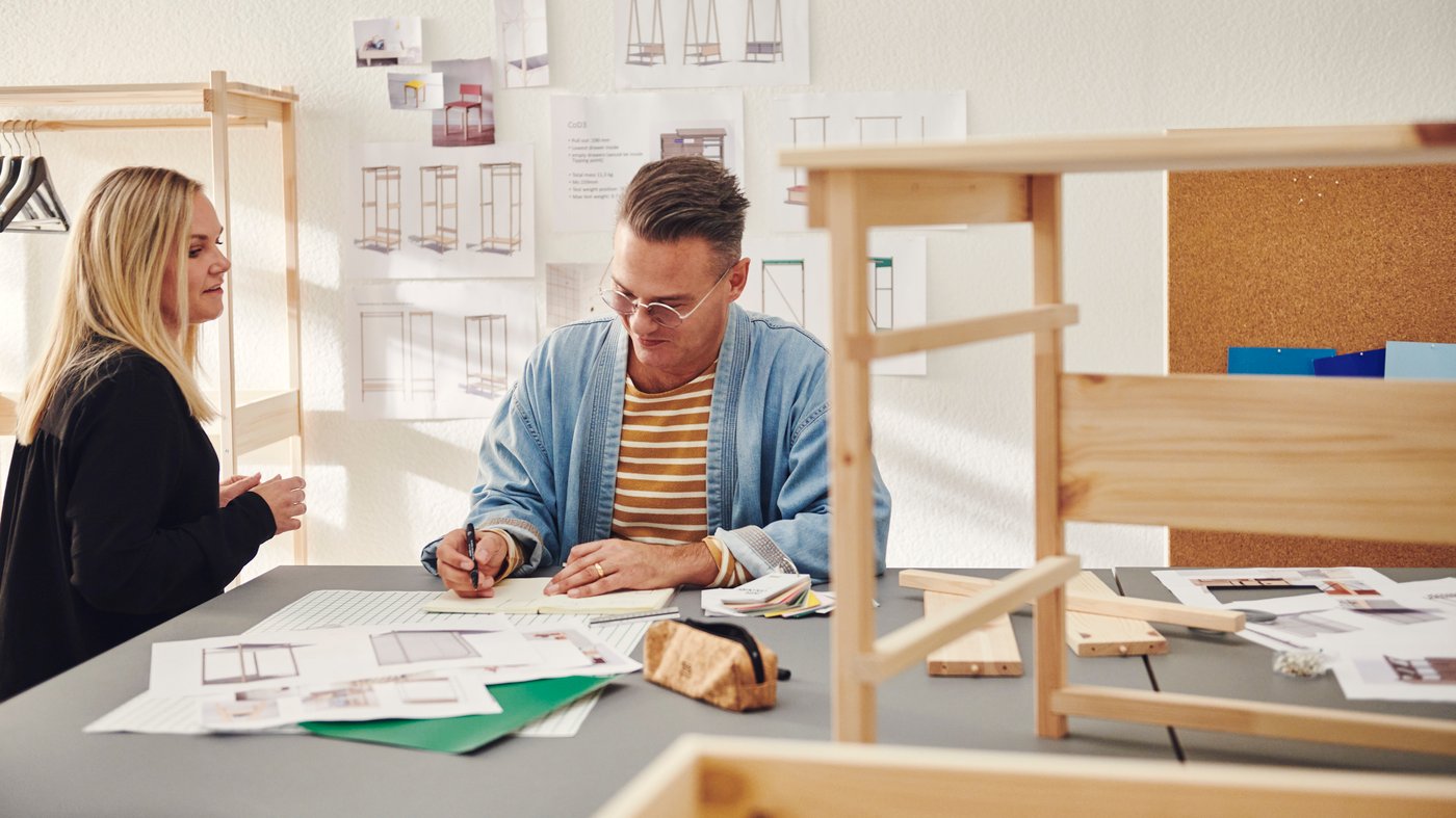 Two IKEA co-workers seated looking at product sketches with a side table prototype on the table nearby.