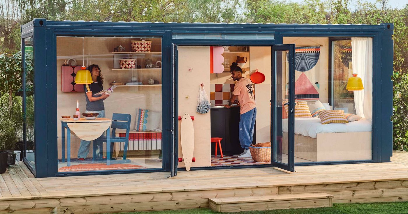 A small, blue and glass fronted home with people in a dining area, kitchen and bedroom. 