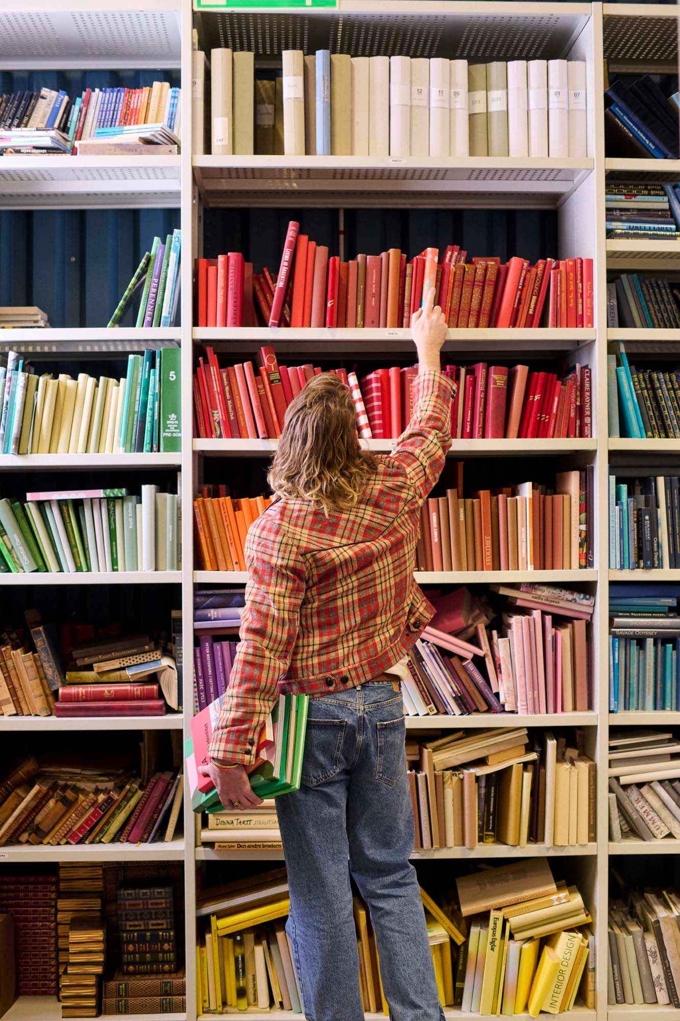 A person reaches up to take a book from a bookshelf.