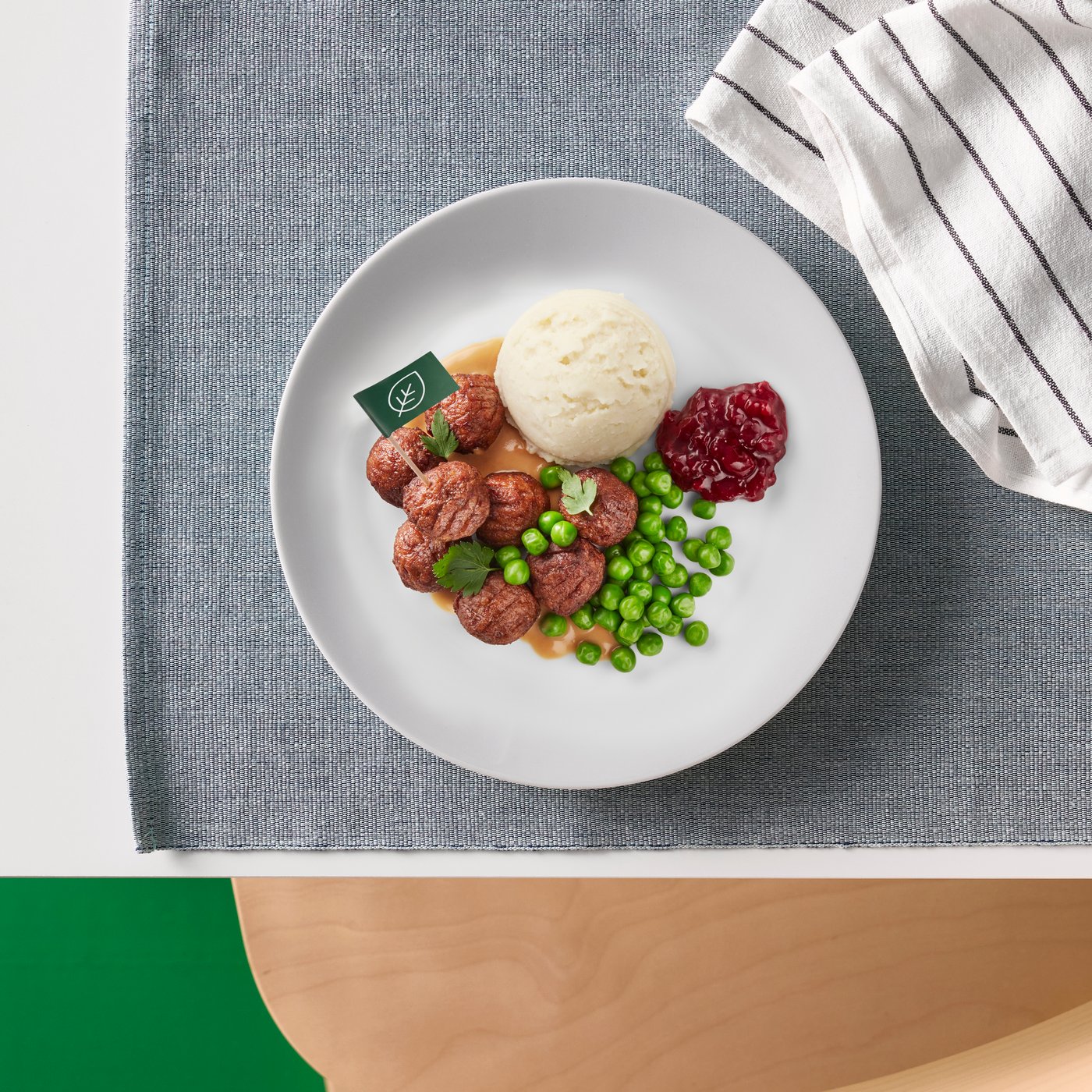 A white plate with meatballs, peas, mashed potatoes and lingonberry sauce rests on a black and white patterned place mat. 