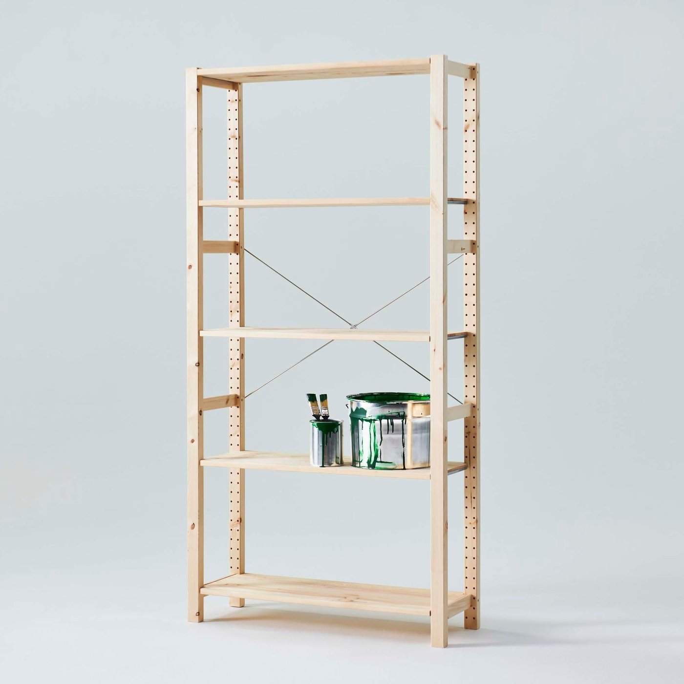 Two paint tins with paint brushes on the second to bottom shelf of an IVAR shelving unit in a light grey environment.