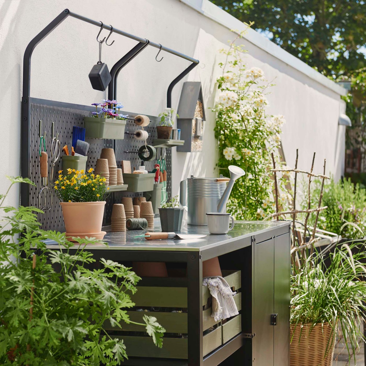 A black outdoor potting station with open and closed storage surrounded by plants. 