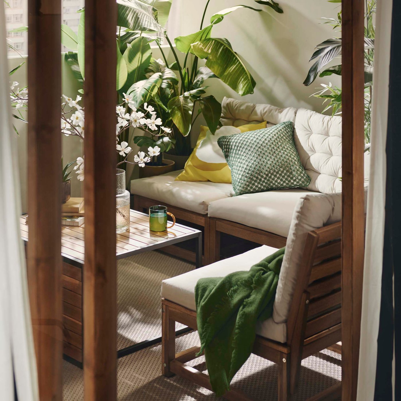 A beige sofa and armchair on a balcony with a wooden coffee table, wood decking and plants.