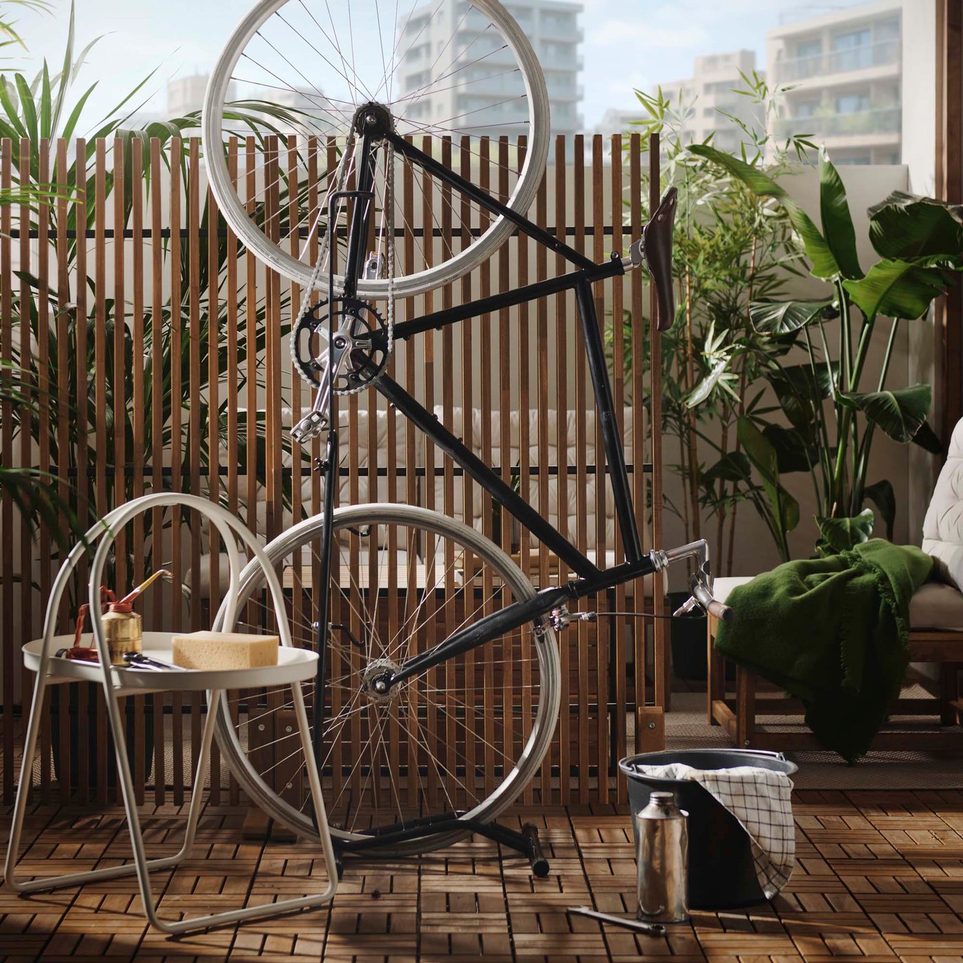 A bicycle is being repaired on a balcony. A seating area with plants can be seen behind a wooden room divider. 