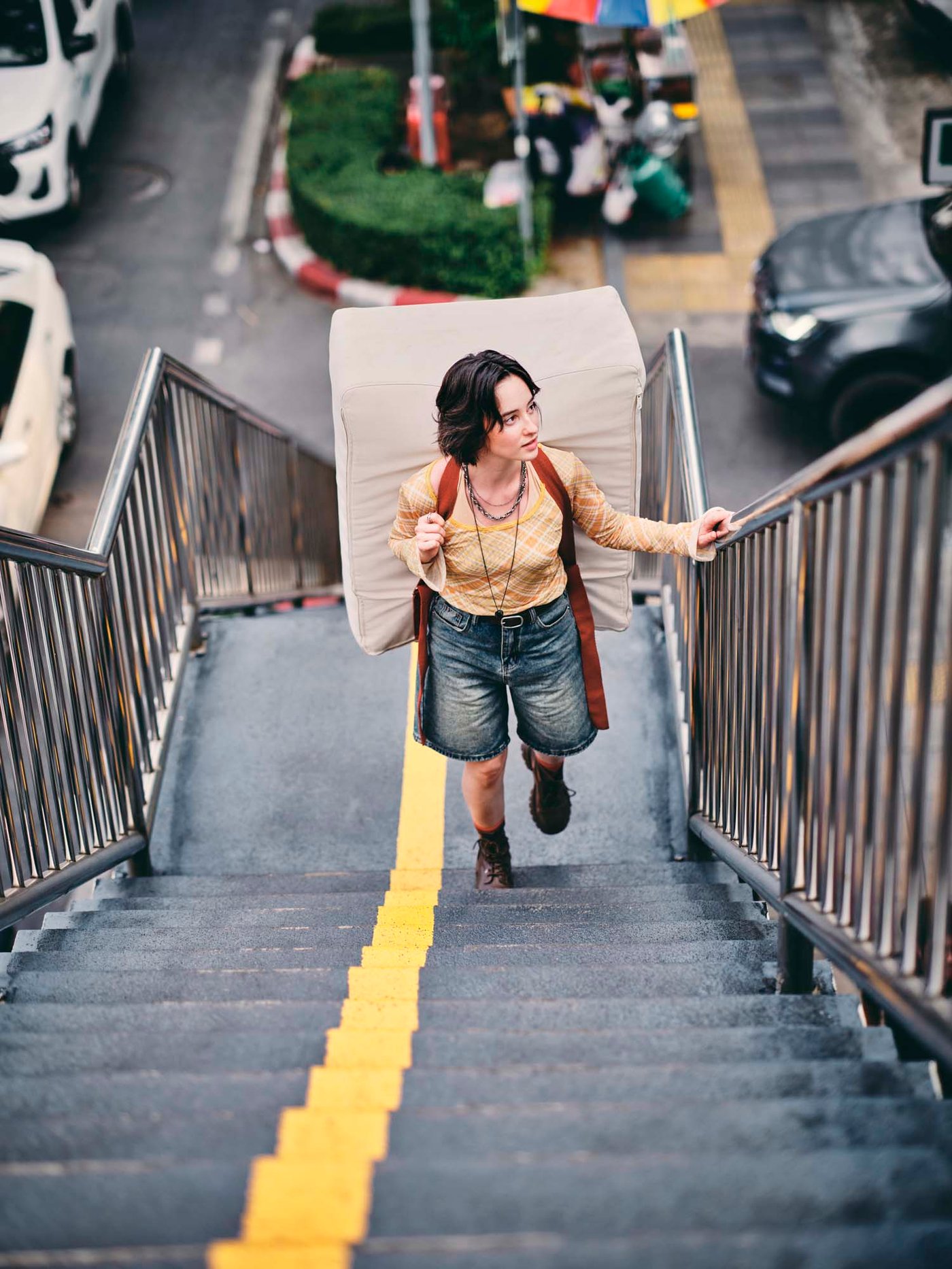 A person climbing stairs with a mattress/pouffe on their back.