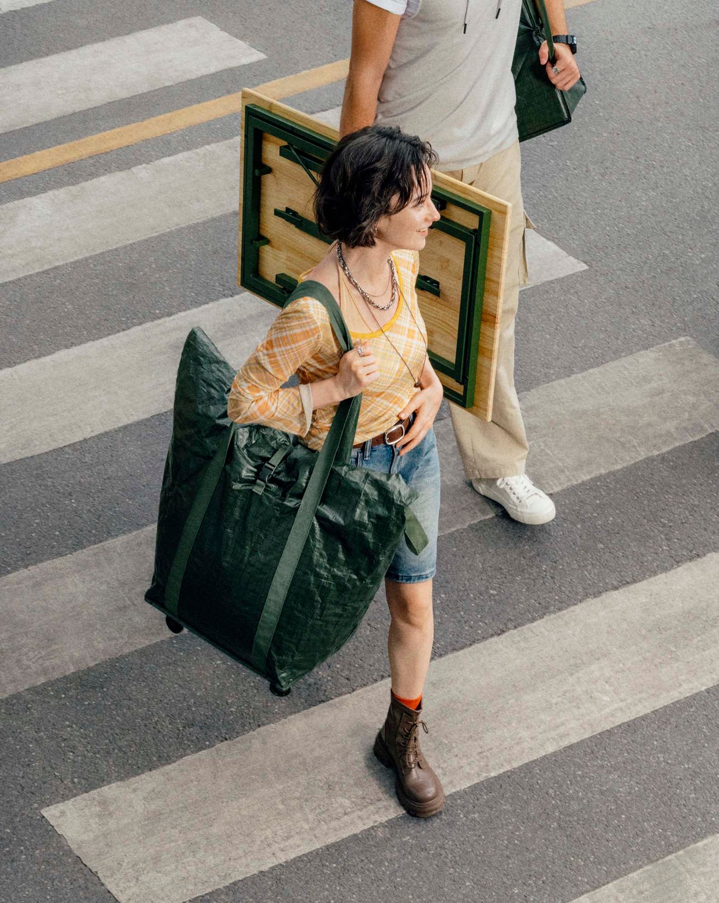 Two people carrying a table and shopping bag over a zebra crossing.