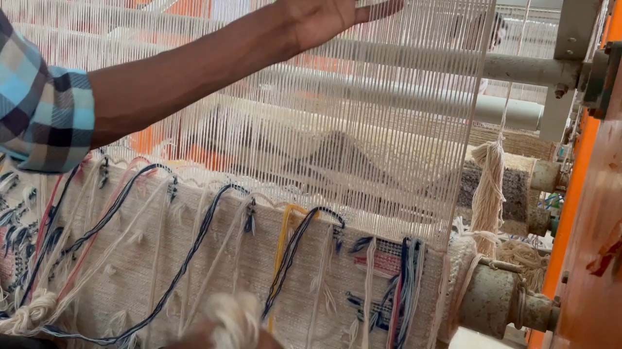 A person sits at a loom, weaving a rug.