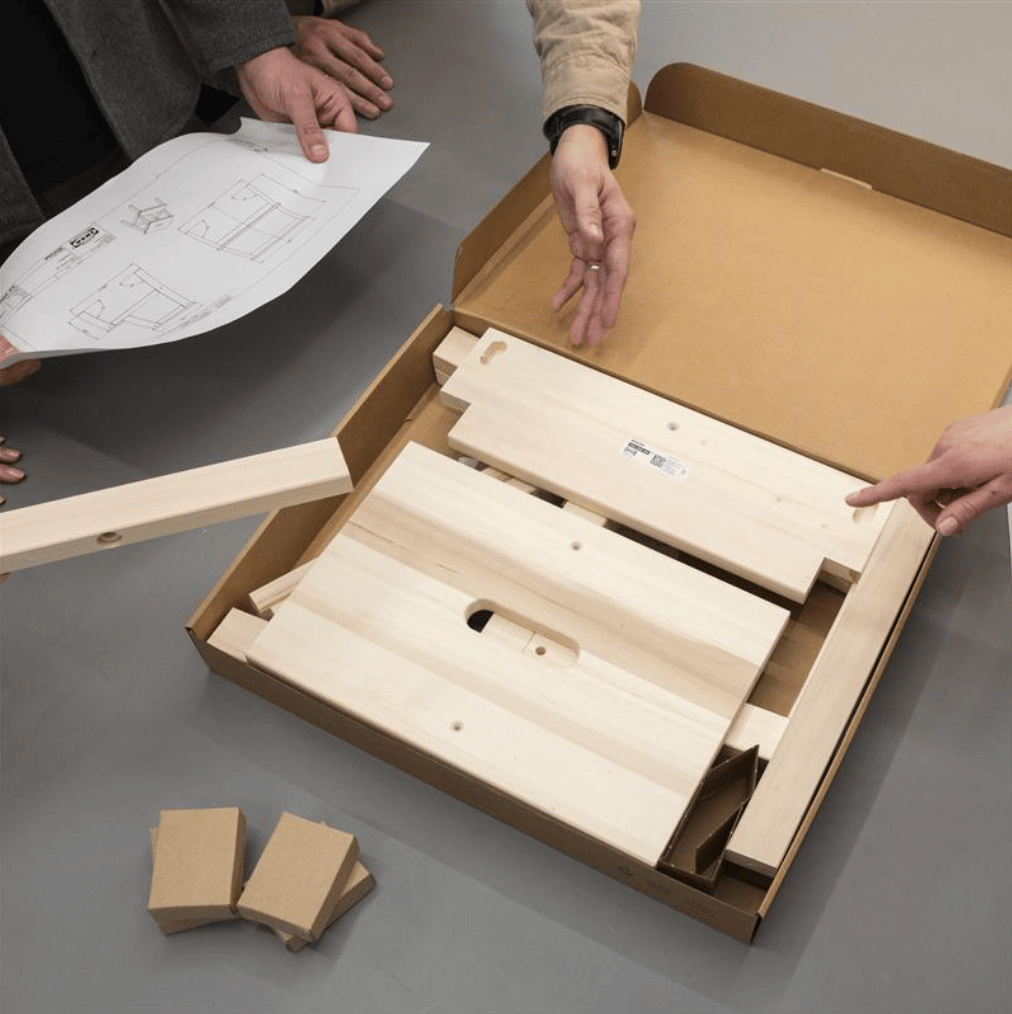 A person holds instructions next to an unassembled product in its packaging with the lid open.