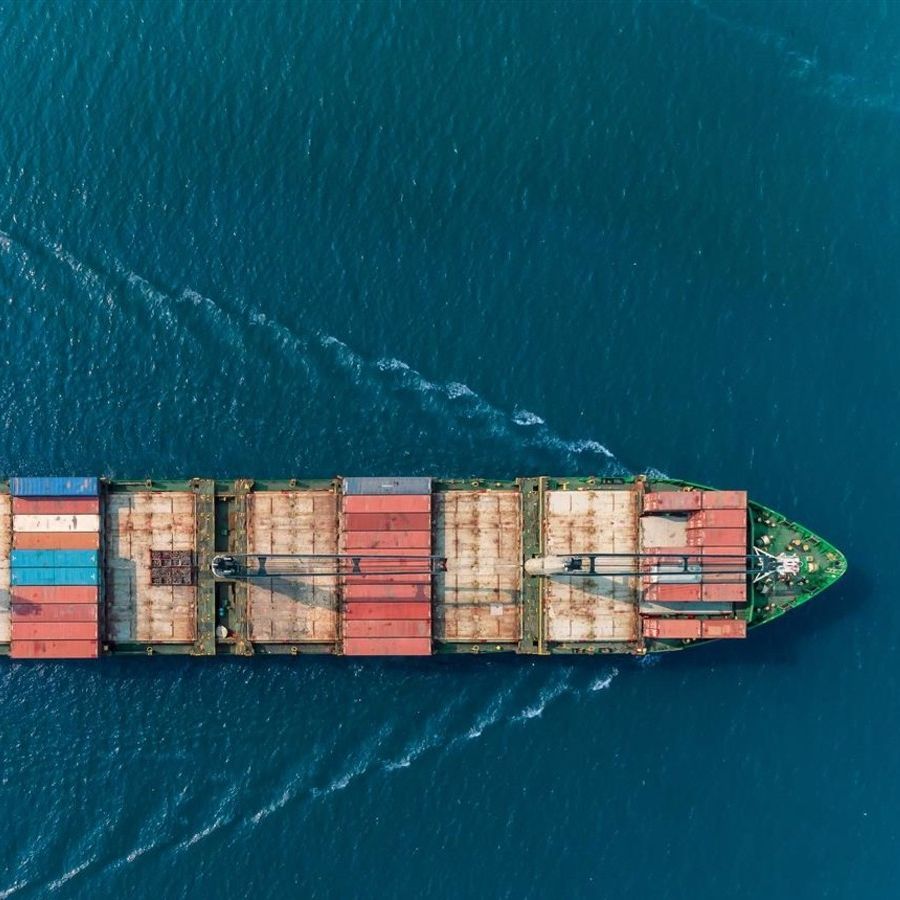 A cargo ship shot from above makes its way across a still, blue ocean.
