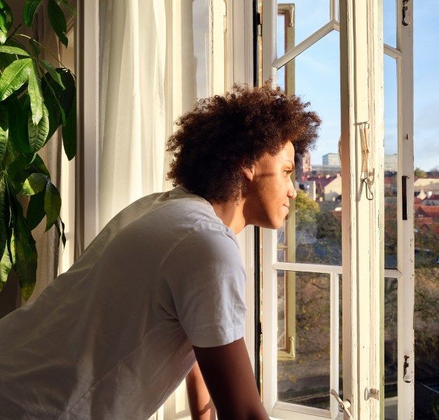 A person looking out of a window with afternoon sunshine coming into the room.