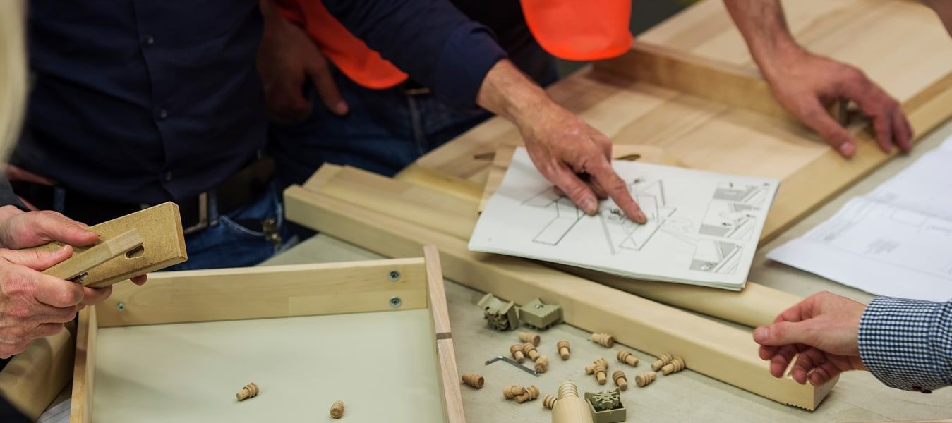 A table with wooden furniture parts and a number of hands holding some of them and pointing at assembly instructions.
