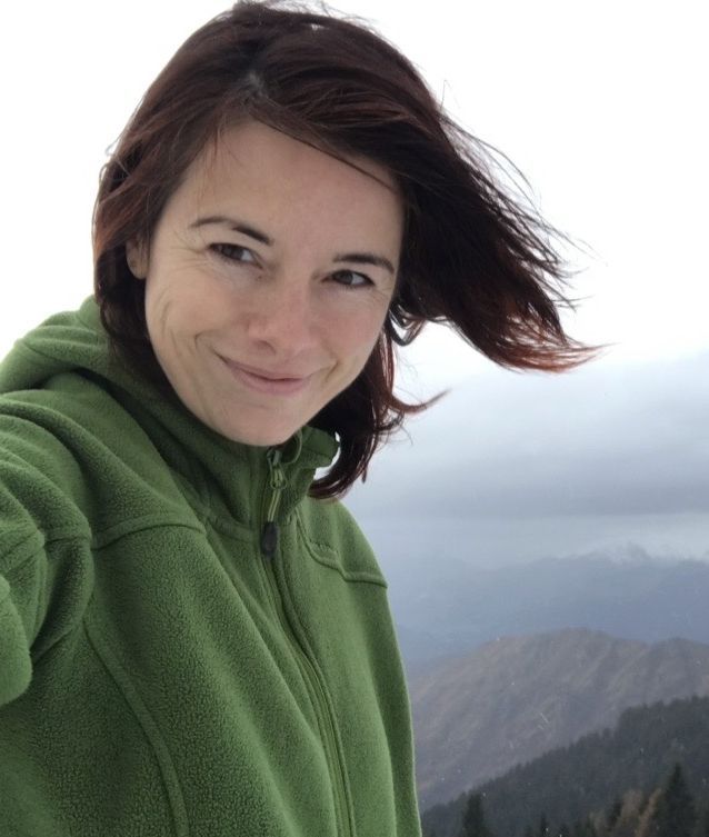 Cristina is outside with nature in the background. She is smiling at the camera.