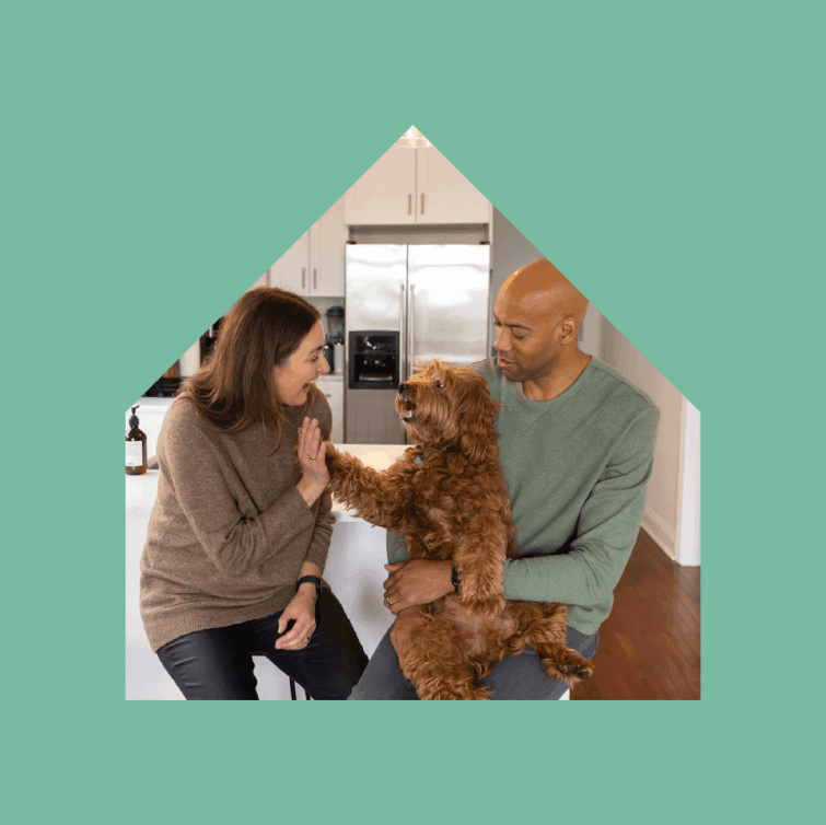 Two people sit in their home. The man has a dog sitting on his lap.