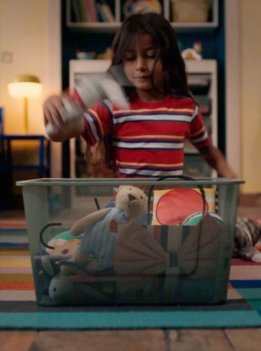 A video still image of a girl sitting on the floor in front of a basket of toys.