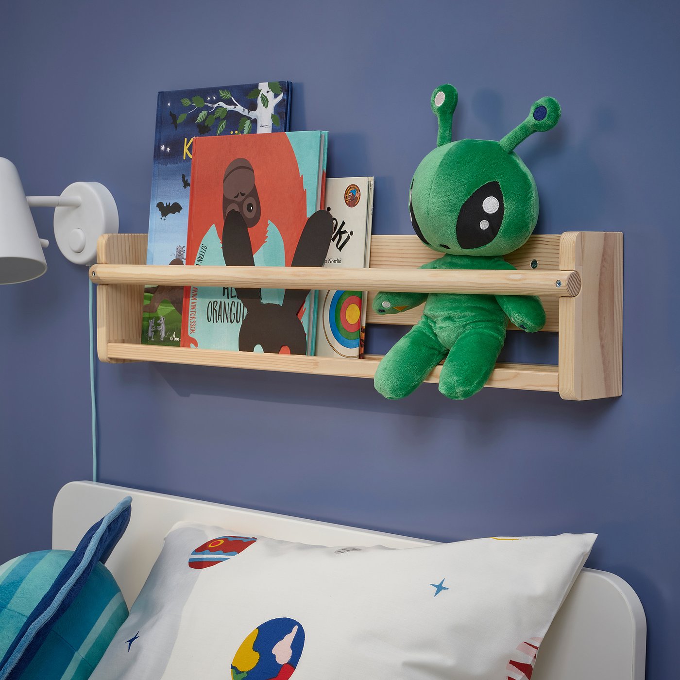 Blue wall with books, alien toy, bed with colourful pillows.